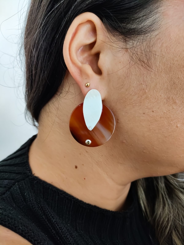 Brinco redondo marrom de pedra com detalhe oval de pérola em orelha feminina.