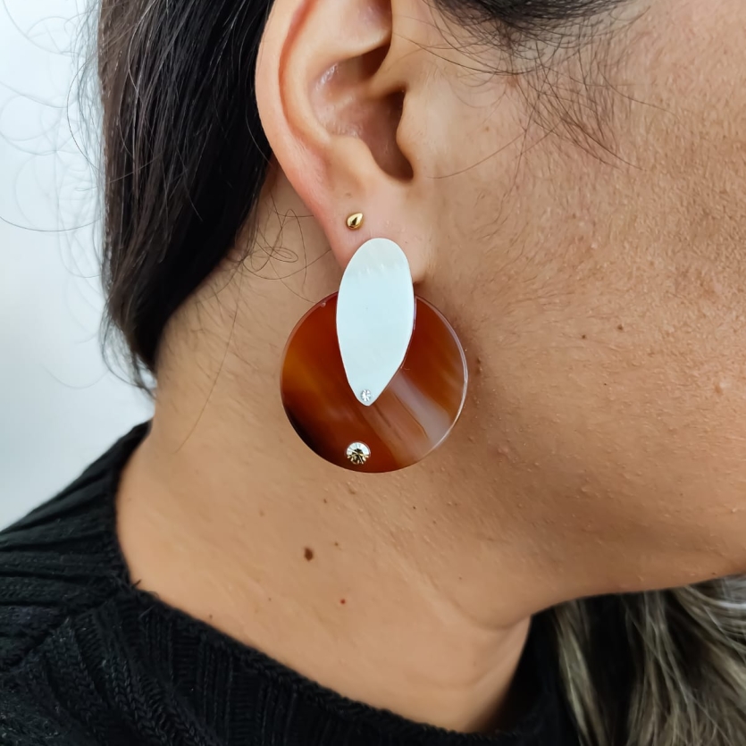 Brinco redondo marrom de pedra com detalhe oval de pérola em orelha feminina.