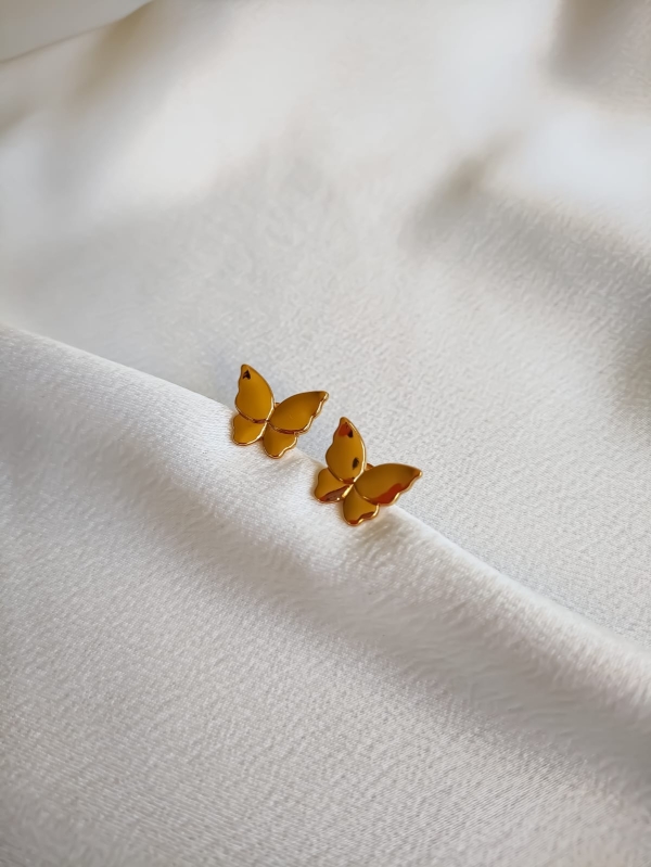 Par de brincos dourados em formato de borboleta sobre tecido branco.