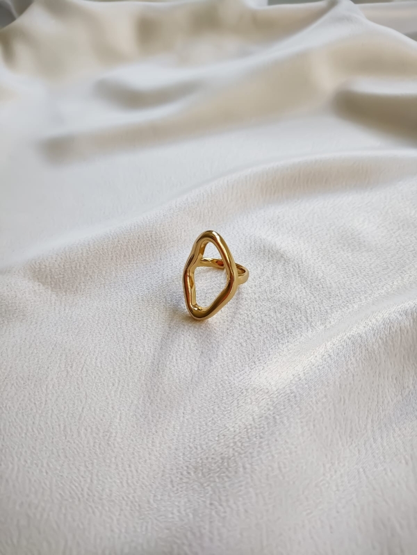 Anel dourado com formato abstrato e acabamento brilhante sobre tecido branco