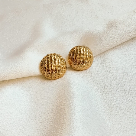 Par de brincos dourados texturizados em formato de esfera sobre tecido branco.