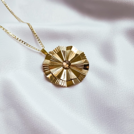 Colar dourado com medalha texturizada sobre tecido branco.