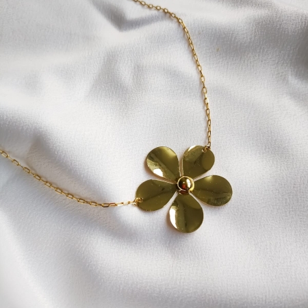 Colar dourado com pingente de flor de cinco pétalas sobre tecido branco.