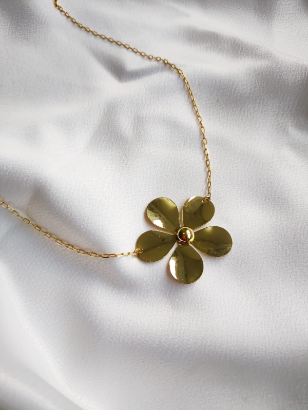 Colar dourado com pingente de flor de cinco pétalas sobre tecido branco.