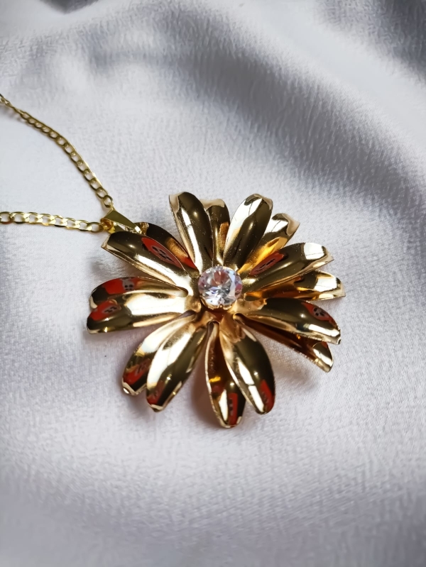 Colar dourado com pingente de flor e centro em cristal sobre fundo branco.