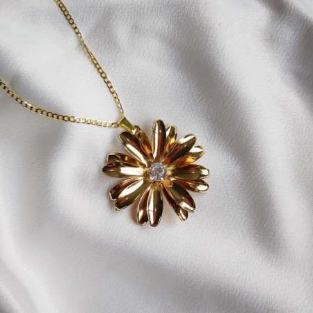 Colar dourado com pingente de flor e centro em cristal sobre fundo branco.