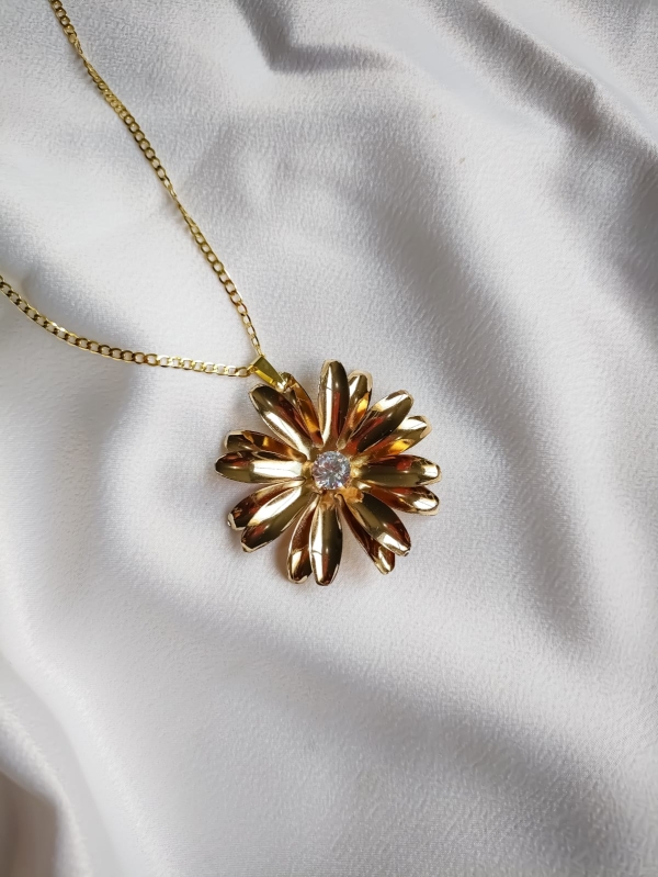Colar dourado com pingente de flor e centro em cristal sobre fundo branco.