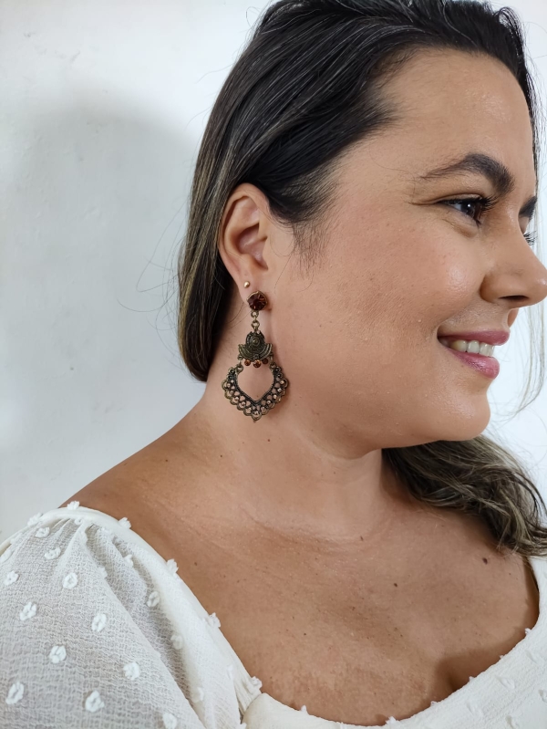 Brinco boho em tom bronze com detalhe em formato de coração vazado e cristais âmbar, usado na orelha feminina.