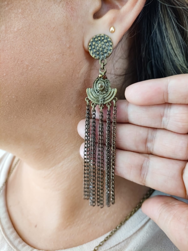 Brinco longo estilo boho com corrente ouro velho e base redonda texturizada, em orelha feminina.