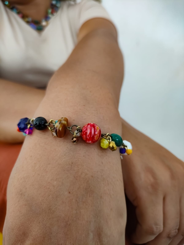 Pulseira com pedrarias coloridas no pulso de uma mulher, com destaque para os detalhes artesanais.