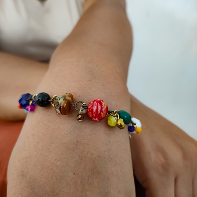 Pulseira com pedrarias coloridas no pulso de uma mulher, com destaque para os detalhes artesanais.