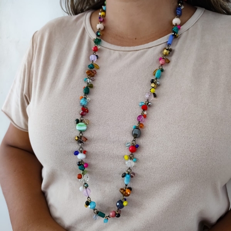 Mulher usando colar longo com pedrarias coloridas e corrente em tom envelhecido.