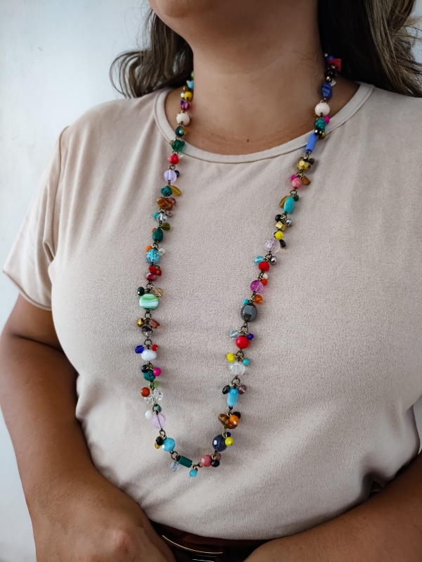 Mulher usando colar longo com pedrarias coloridas e corrente em tom envelhecido.