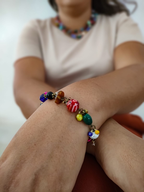 Pulseira com pedrarias coloridas no pulso de uma mulher, com destaque para os detalhes artesanais.