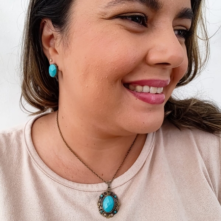 Mulher usando colar com pingente oval azul turquesa e brinco combinando, ambos em estilo vintage.