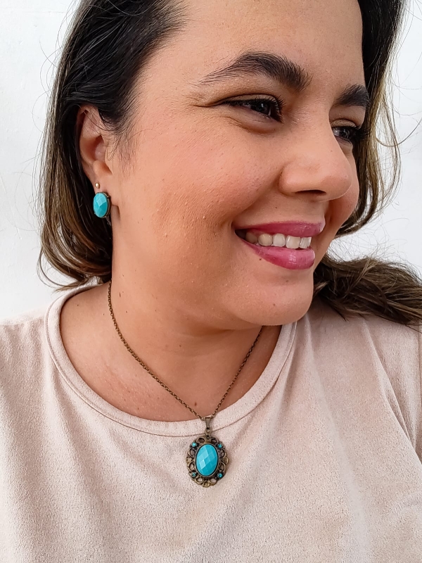 Mulher usando colar com pingente oval azul turquesa e brinco combinando, ambos em estilo vintage.