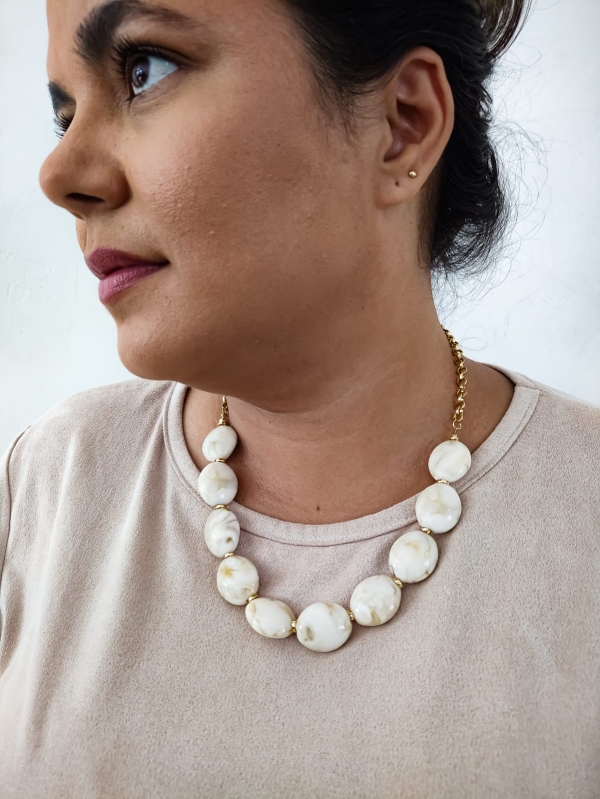 Mulher usando colar de resina com contas grandes em tom marfim e fecho dourado, visual clássico e refinado.