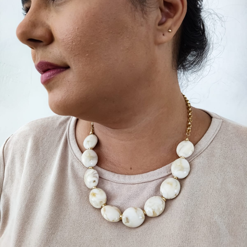 Mulher usando colar de resina com contas grandes em tom marfim e fecho dourado, visual clássico e refinado.