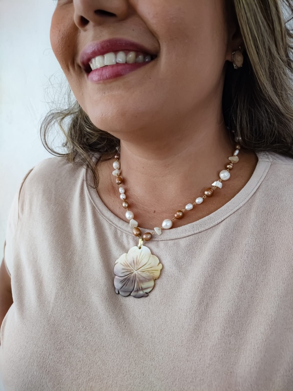 Colar boho com pérolas resinadas e pingente floral de madrepérola usado por mulher de blusa clara.