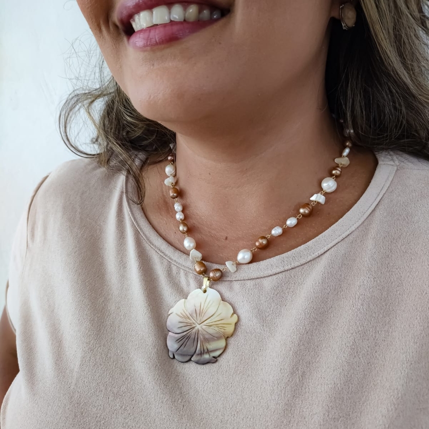 Colar boho com pérolas resinadas e pingente floral de madrepérola usado por mulher de blusa clara.
