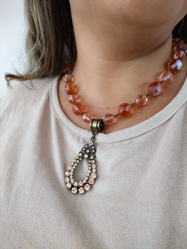 Colar boho com contas de cristal rosado e pingente vintage com strass usado por mulher de blusa clara.