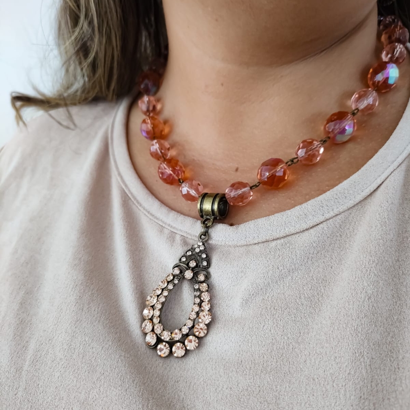 Colar boho com contas de cristal rosado e pingente vintage com strass usado por mulher de blusa clara.