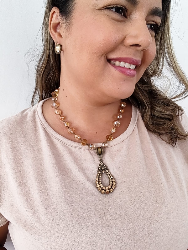 Colar boho com contas de cristal rosado e pingente vintage com strass usado por mulher de blusa clara.