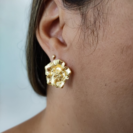 Brinco dourado em formato de flor com textura detalhada usado por mulher.
