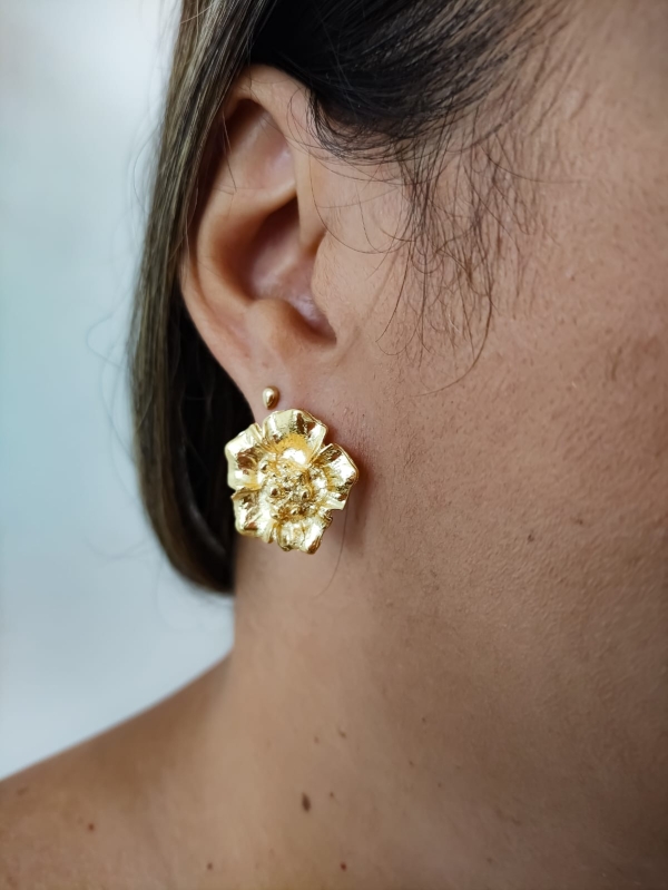 Brinco dourado em formato de flor com textura detalhada usado por mulher.