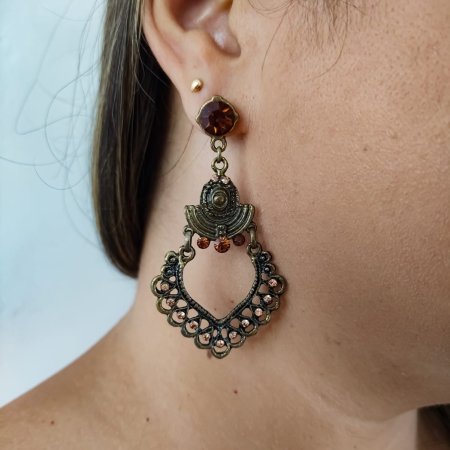 Brinco boho em tom bronze com detalhe em formato de coração vazado e cristais âmbar, usado na orelha feminina.