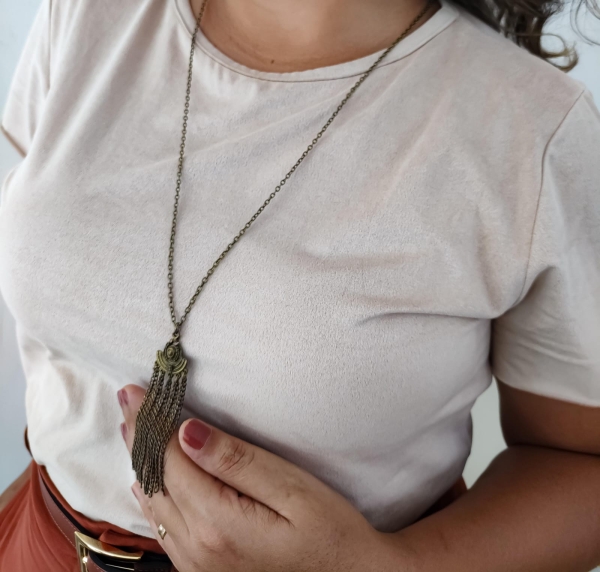 Colar longo com pingente bronze e correntes finas estilo boho, usado sobre blusa bege.