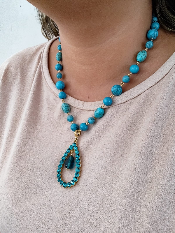 Colar boho azul com pedras turquesa e pingente em forma de gota, usado por mulher sorridente.