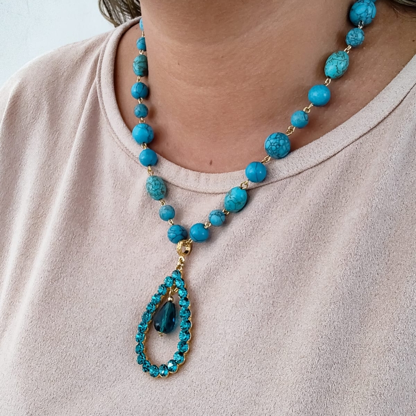 Colar boho azul com pedras turquesa e pingente em forma de gota, usado por mulher sorridente.