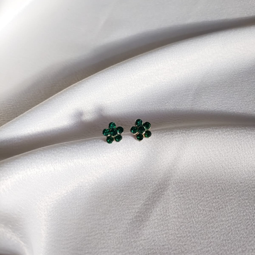 Par de brincos pequenos em formato de flor com strass verde, sobre tecido branco acetinado.