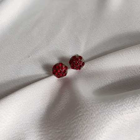 Par de brincos pequenos em formato de flor com strass vermelho, sobre tecido branco acetinado.