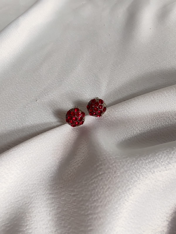 Par de brincos pequenos em formato de flor com strass vermelho, sobre tecido branco acetinado.