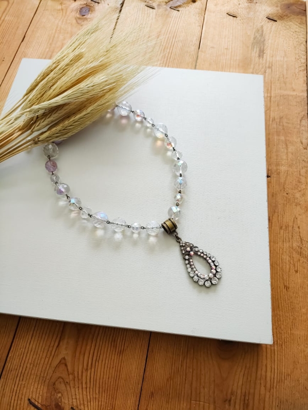 Colar boho com cristais em tons de âmbar e caramelo, com pingente vintage oval e fundo branco decorado com ramo de trigo.