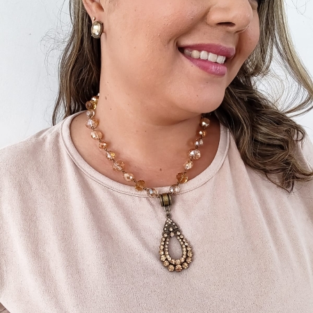 Colar boho com cristais em tons de âmbar e caramelo, com pingente vintage oval e fundo branco decorado com ramo de trigo.