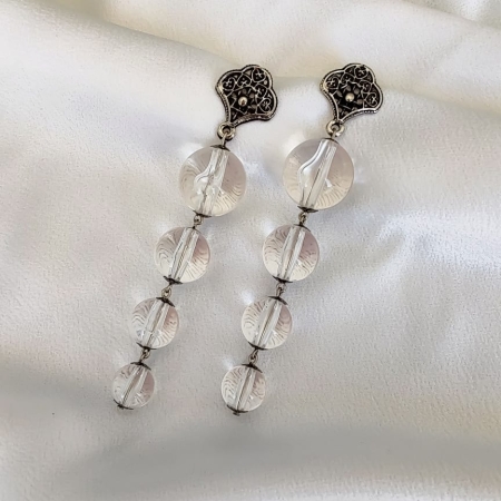 Brinco longo com contas transparentes lapidadas e base metálica trabalhada com detalhes vazados.