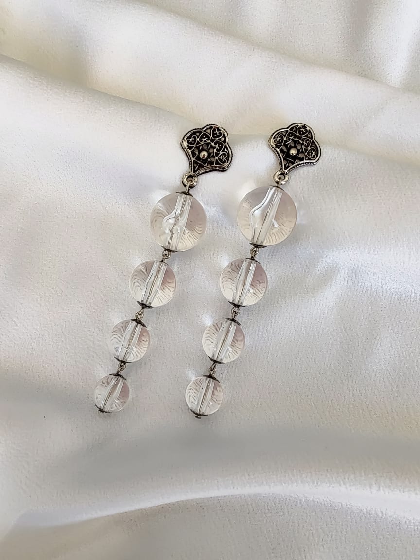 Brinco longo com contas transparentes lapidadas e base metálica trabalhada com detalhes vazados.