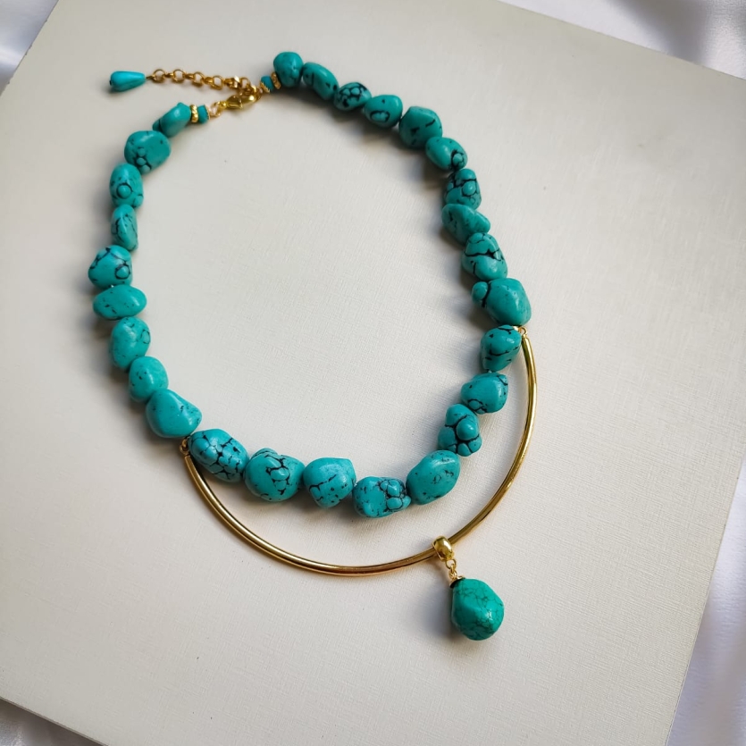 Colar de pedras turquesa irregulares com arco metálico dourado e pingente de pedra turquesa.