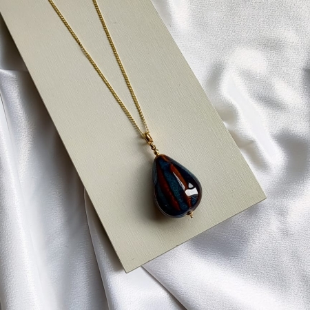 Colar longo dourado com pingente em formato de gota azul com detalhes em marrom.