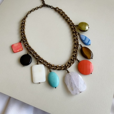 Maxi colar com corrente dourada e pedras coloridas de diferentes formatos penduradas como pingentes.