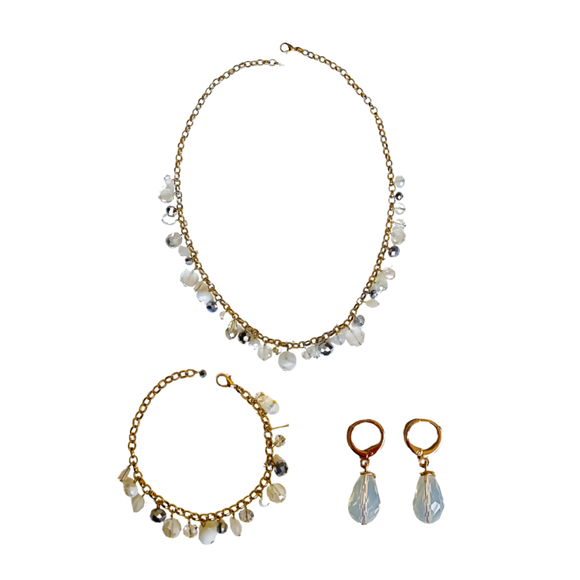 Conjunto feminino com colar, pulseira e brincos dourados com pedrarias brancas e transparentes, design delicado e acabamento artesanal.